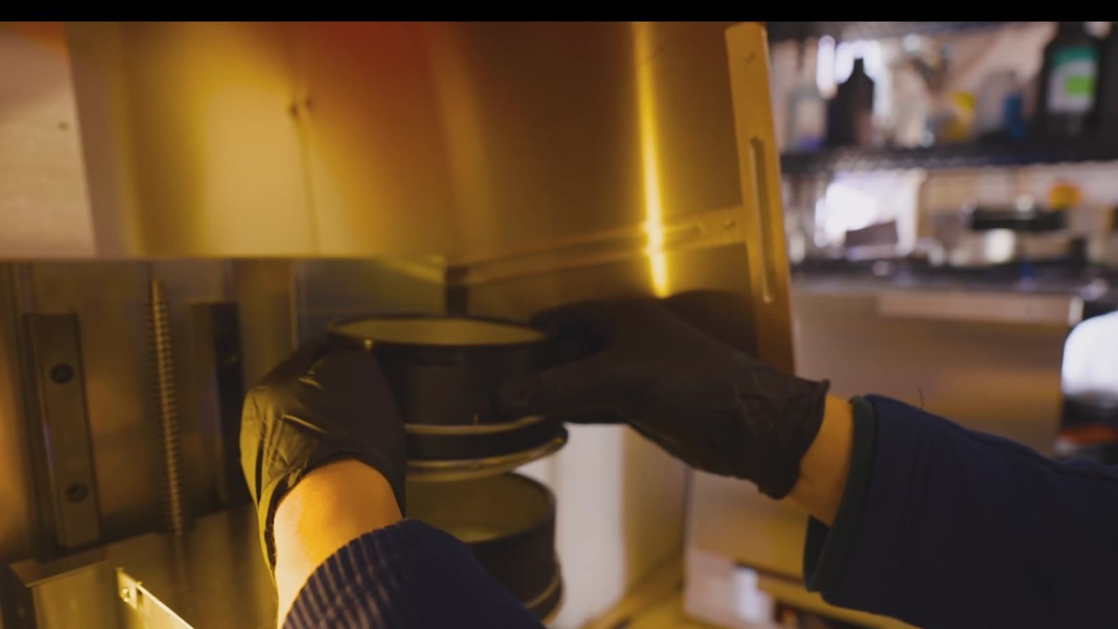 Gloved hands loading a material canister into the printer.