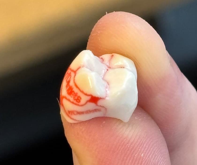 A printed crown held between two fingers, with a second material placed as fine red detail across the white body.